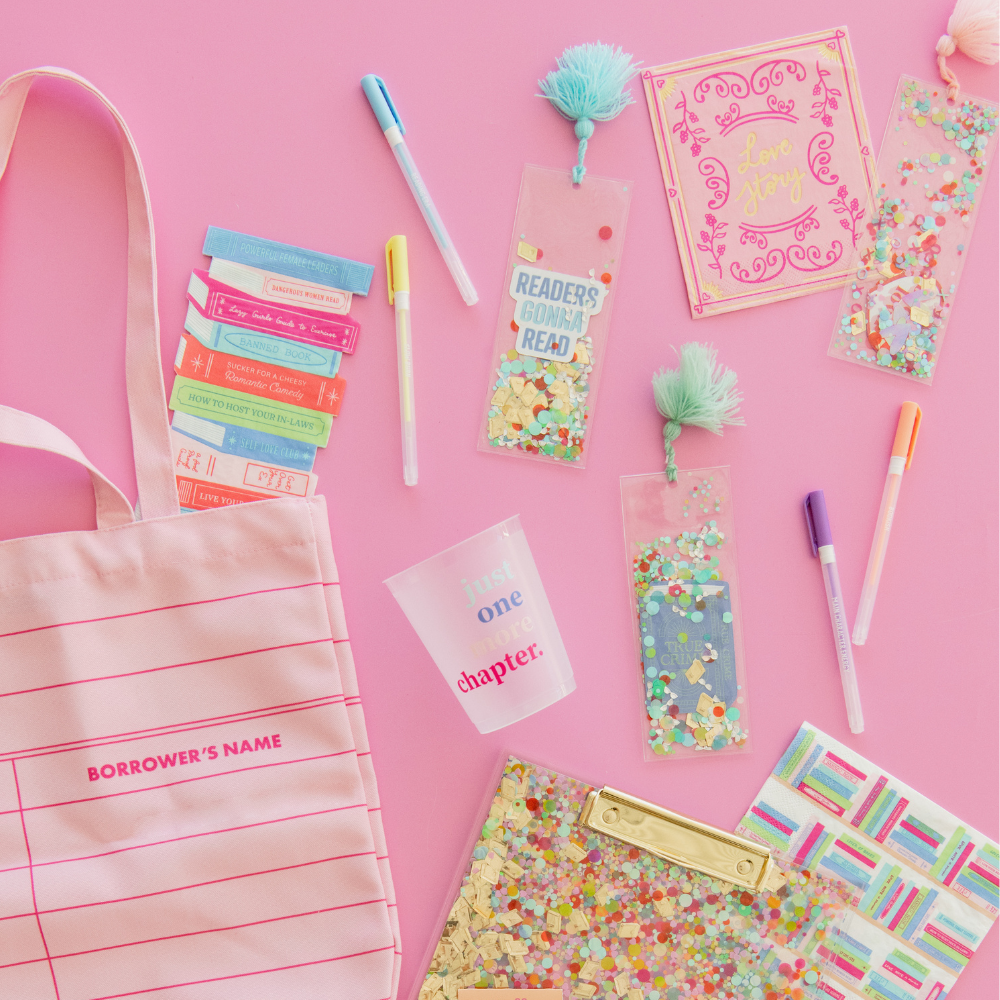 Confetti bookmarks with pink and aqua tassels on a pink table beside a tote bag, pens and a clutch