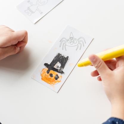Child coloring a spider and a pumpkin witch hat cling with a yellow crayon