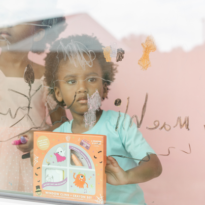 Child in a teal shirt holding the Monster Mash box in front of a window with crayon drawings