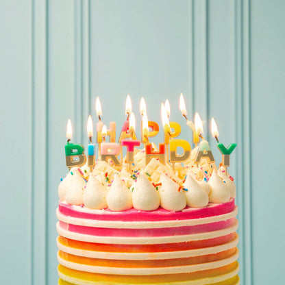 Lit rainbow letter candles spelling Happy Birthday on a cake with pink and orange stripes