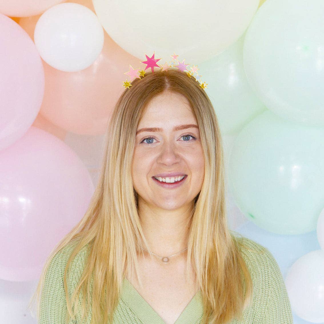 Woman in a green sweater smiling in the star headband in front of pastel balloons