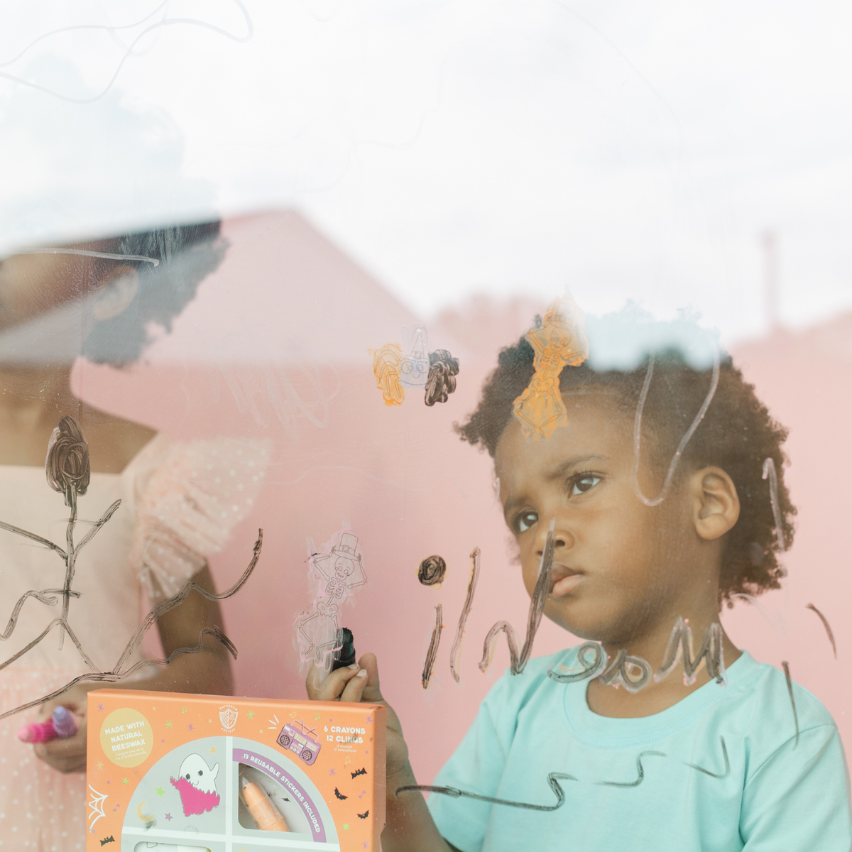Child at a window drawing with crayons beside the Monster Mash box