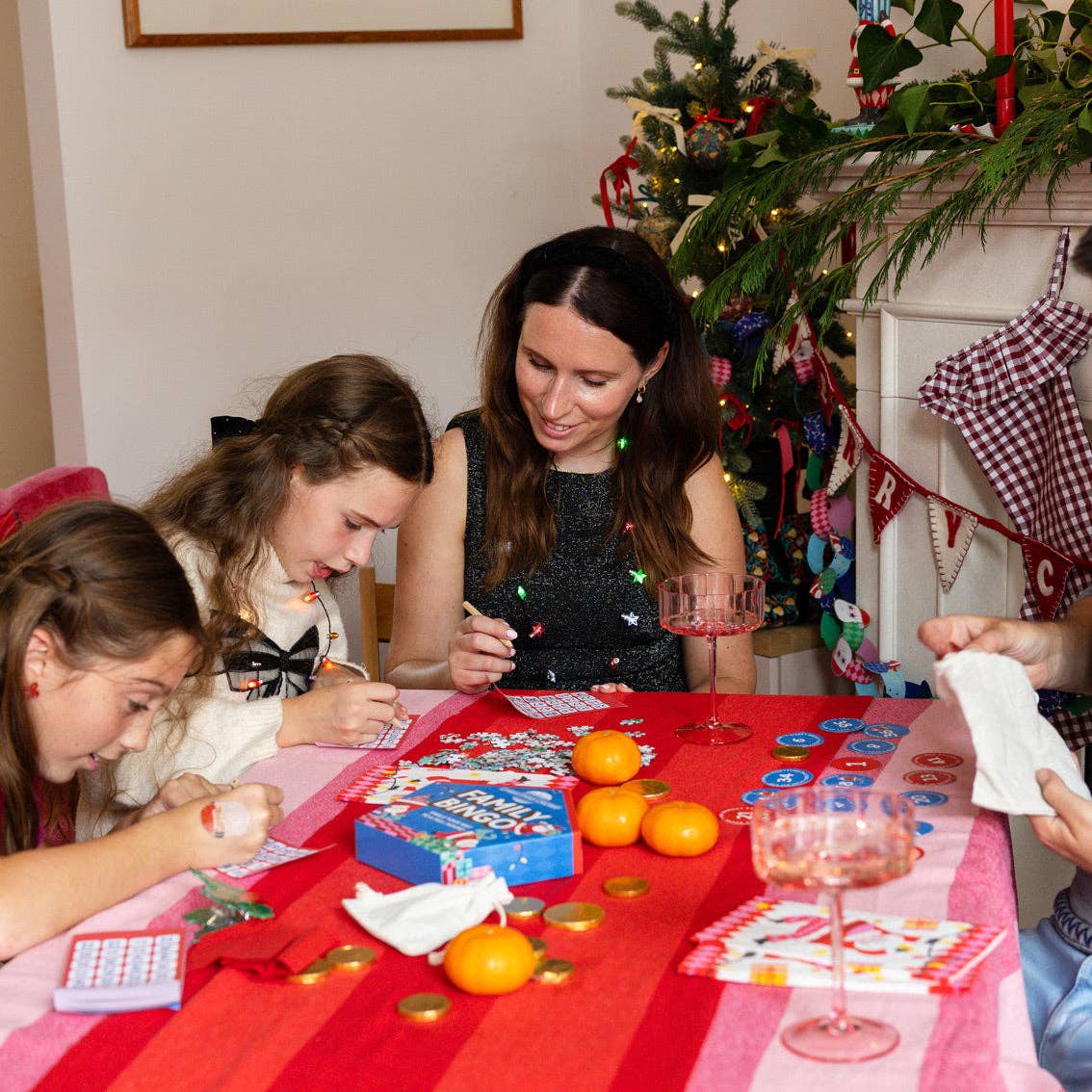 Family playing bingo at a red table with oranges and a pink glass near a Christmas tree