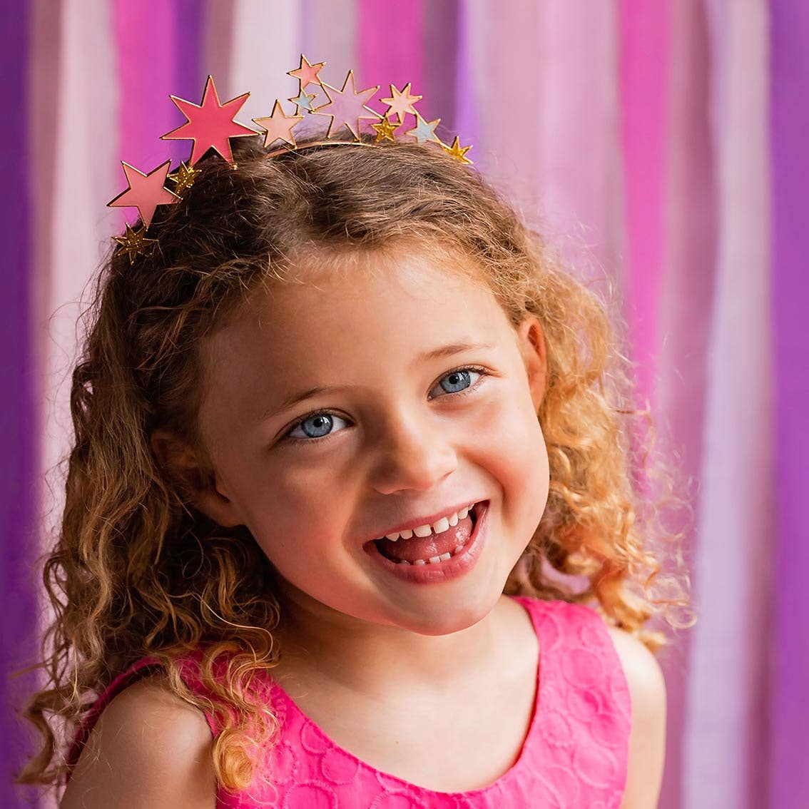 Smiling girl wearing the star headband in front of pink and purple streamers