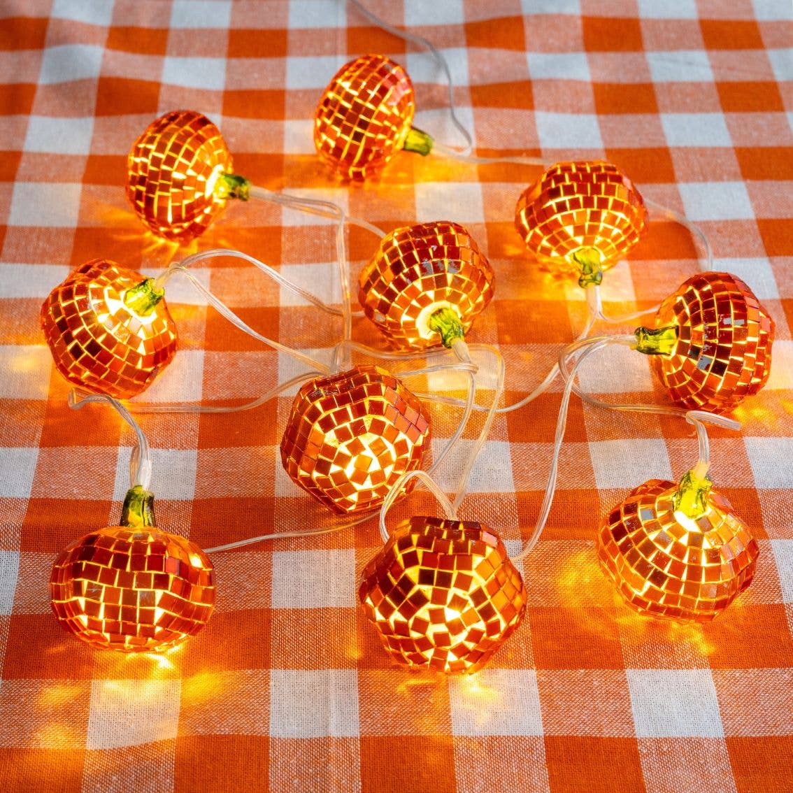Lit mirror-ball pumpkins glowing amber on an orange and white gingham tablecloth
