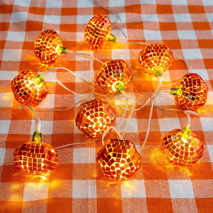 Lit mirror-ball pumpkins glowing amber on an orange and white gingham tablecloth