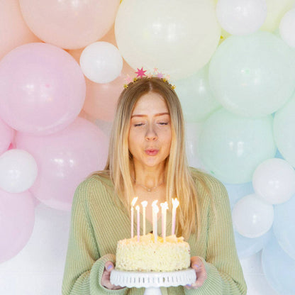 Woman in a green sweater wearing the star headband and holding a lit birthday cake