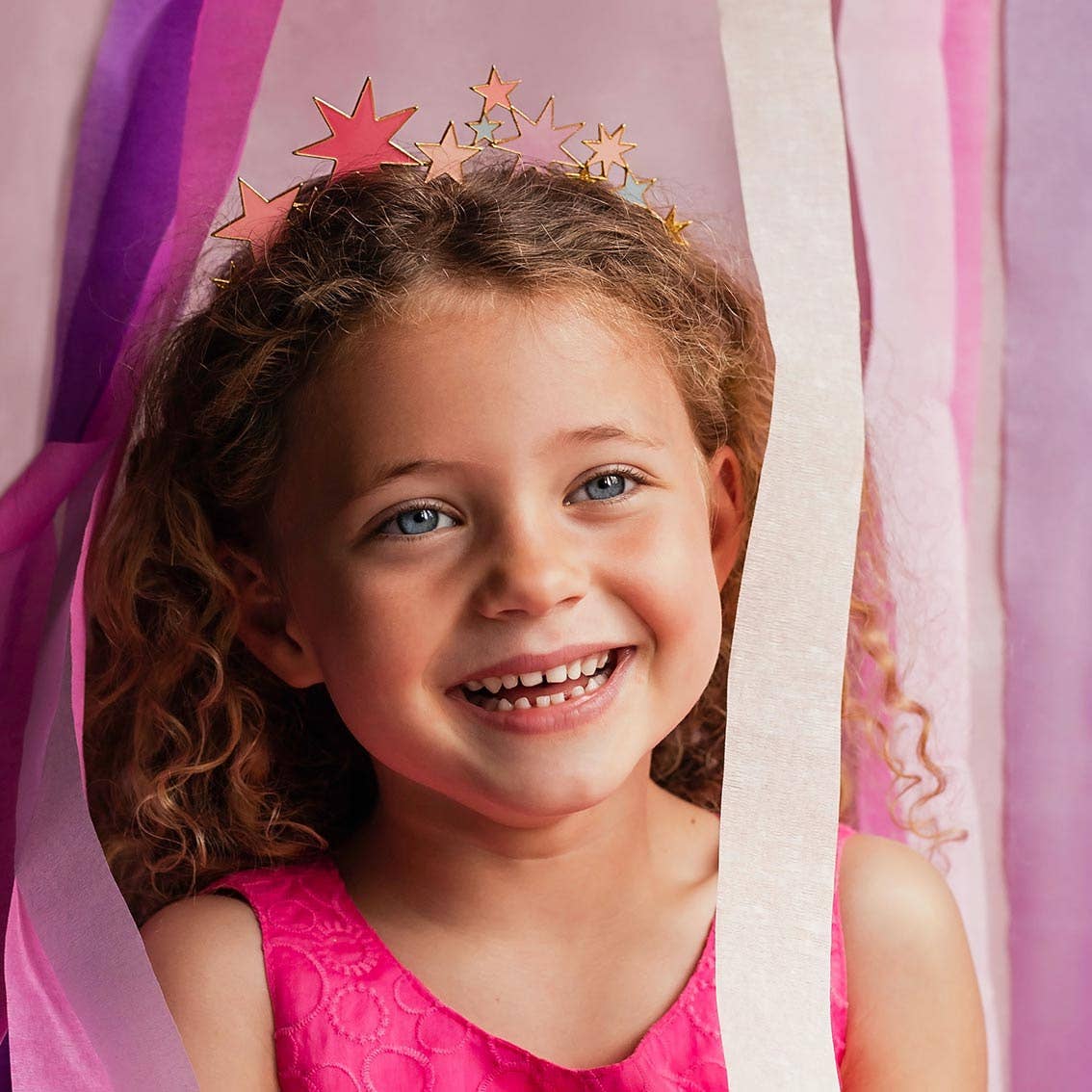 Girl with curly hair grinning in the star headband beside cream streamers